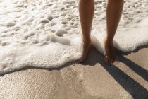 Sección baja de mujer bronceada de pie en la playa en un día soleado. Ella está caminando. - foto de stock