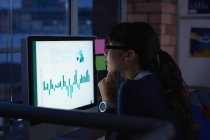 Seitenansicht einer Geschäftsfrau, die nachts im Büro am Schreibtisch an einem Graphenprojekt arbeitet — Stockfoto