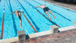 Высокий угол обзора мужчин и женщин кавказских пловцов, прыгающих в воду в одно и то же время у бассейна под солнцем — стоковое фото