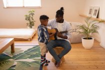 Вид на счастливых отца и сына афроамериканцев, играющих дома на гитаре — стоковое фото