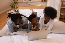 Vista frontal da família afro-americana feliz juntos desfrutando ao usar o laptop em casa. Estão a sorrir. — Fotografia de Stock