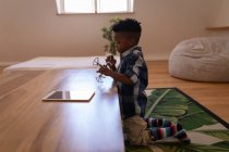 Vue latérale du petit garçon afro-américain mignon jouant avec un drone à la maison — Photo de stock
