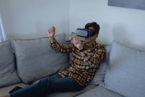 Vista frontal do jovem homem caucasiano usando fone de ouvido realidade virtual em casa — Fotografia de Stock