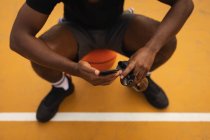 Baixa seção de jogador relaxante na quadra de basquete ao usar o telefone móvel — Fotografia de Stock