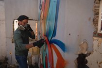 Vista laterale del giovane artista graffiti caucasici pittura a spruzzo sulla parete intemperie — Foto stock