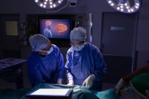 Vista frontal de cirurgiões concentrados realizando operação em centro cirúrgico no hospital contra manchas e tela digital em segundo plano — Fotografia de Stock