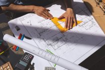 High angle view of male architect working on blueprint with triangle ruler at desk in a modern office — Stock Photo
