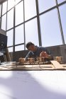 Vue de face de l'architecte asiatique mâle travaillant sur un modèle d'immeuble de bureaux avec son ordinateur portable et ses outils dans un bureau moderne — Photo de stock