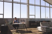 Vorderansicht eines fleißigen asiatischen männlichen Architekten, der am Schreibtisch sitzt und in einem modernen Büro mit dem Handy telefoniert — Stockfoto