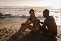 Vue latérale du jeune homme afro-américain appliquant de la crème solaire à une femme sur le dos — Photo de stock