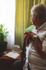 Vue latérale de l'homme caucasien âgé regardant par la fenêtre tout en étant assis seul sur le lit à la maison de soins infirmiers. Il se penche contre le bâton . — Photo de stock