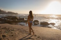 Вид ззаду жінки, що ходить на пляжі в сонячний день — стокове фото
