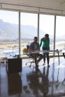 Vista frontale di architetti caucasici che interagiscono su cianografie in ufficio contro bella vista. Architetto maschio seduto sulla sedia mentre architetto donna in piedi — Foto stock