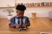Vista frontal de un niño afroamericano lindo jugando con un dron en casa - foto de stock