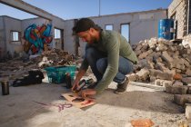 Seitenansicht junger kaukasischer Graffiti-Künstler sprüht Malerei auf Karton in der Gasse — Stockfoto