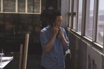 Вид азиатского архитектора-мужчины, разговаривающего по мобильному телефону в современном офисе — стоковое фото
