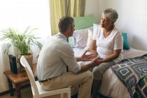 Vue en angle élevé du médecin masculin caucasien interagissant avec une patiente âgée de race mixte à la maison de retraite — Photo de stock