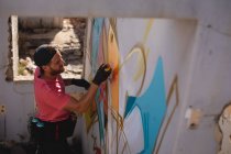 High angle view of young Caucasian graffiti artist spray painting on weathered wall room — Stock Photo
