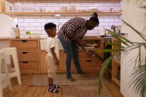 Vue latérale du bel homme afro-américain insérant une pizza dans un four à la cuisine de la maison tandis que son fils debout à l'arrière — Photo de stock