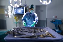 Front view of surgical equipment on an table in operation room at hospital with surgeon in the background — Stock Photo