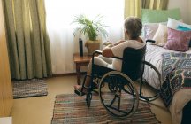Задний вид на заботливую пожилую женщину-инвалида, сидящую в инвалидной коляске в спальне в доме престарелых — стоковое фото