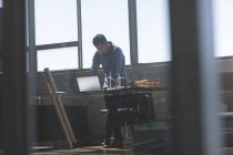 Vista frontal del arquitecto asiático trabajando sobre el portátil en el escritorio en una oficina moderna - foto de stock