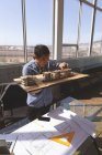 Vista frontal do arquiteto asiático masculino segurando um modelo de edifício arquitetônico e trabalhando nele na mesa em um escritório moderno — Fotografia de Stock