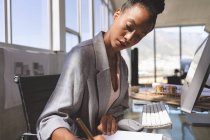 Seitenansicht einer jungen Geschäftsfrau mit gemischter Rasse, die am Schreibtisch im Büro auf einem Notizblock am Computer arbeitet — Stockfoto