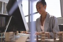 Niederwinkelblick lächelnd gemischte Geschäftsfrau, die am Computer am Schreibtisch im Büro arbeitet — Stockfoto