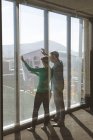 Visão traseira de arquitetos caucasianos segurando planta contra uma janela e discutindo sobre isso no escritório — Fotografia de Stock