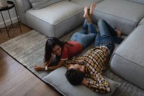Високий кут зору молодої багатоетнічної пари, що взаємодіє один з одним, лежачи на підлозі вдома — стокове фото