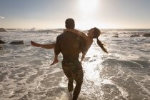 Rückansicht eines jungen Paares, das an einem sonnigen Tag am Strand genießt — Stockfoto