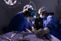 Low angle view of surgeons concentrated performing operation in operating room at hospital with scissors in foreground — Stock Photo