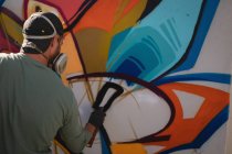 Заднього вигляду молодих кавказьких художника графіті аерозольних розпис по вивітрюванню стіни кімнати — стокове фото