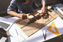 Hochwinkelaufnahme eines asiatischen männlichen Architekten, der am Schreibtisch in einem modernen Büro an einem Architekturmodell arbeitet — Stockfoto