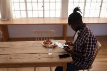 Вид сбоку на красивого афроамериканца, сидящего дома на стуле с цифровым планшетом — стоковое фото