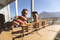 Front view of Caucasian architects discussing over architectural model while male architect touches the model against beautiful view — Stock Photo
