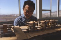 Вигляд спереду чоловічого азіатських архітектора, дивлячись на архітектурно-будівельна модель в сучасні офісні — стокове фото