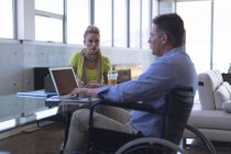 Ejecutivo caucásico discapacitado masculino y femenino caucásico interactuando entre sí en la oficina - foto de stock