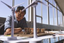 Vorderseite eines asiatischen männlichen Architekten, der ein Architekturmodell auf dem Schreibtisch in einem modernen Büro betrachtet — Stockfoto