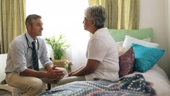 Вид сбоку врача-кавказца, взаимодействующего с пациенткой пожилой смешанной расы в доме престарелых — стоковое фото