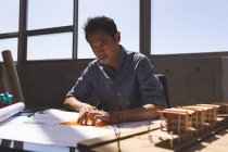 Вид спереди красивого азиатского архитектора-мужчины, работающего на голубом принте с треугольным рулером и карандашом за столом в современном офисе — стоковое фото