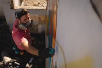 Vista de alto ângulo do jovem artista de grafite caucasiano pintura por pulverização na sala de parede resistida — Fotografia de Stock