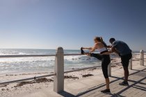 Vista lateral de la joven pareja multiétnica que hace ejercicio cerca de la playa en el paseo marítimo - foto de stock
