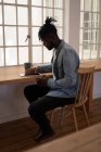 Seitenansicht eines afrikanisch-amerikanischen Mannes, der zu Hause auf einem Stuhl sitzt und ein digitales Tablet benutzt — Stockfoto
