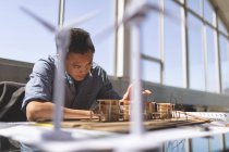 Vorderseite eines asiatischen männlichen Architekten, der am Schreibtisch in einem modernen Büro an einem Architekturmodell arbeitet — Stockfoto