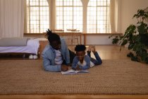 Vue de face du père et du fils afro-américains heureux lisant le livre alors qu'ils étaient couchés sur le sol à la maison — Photo de stock