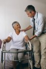 Front view of Caucasian male doctor helping senior mixed race female patient to walk with walker — Stock Photo