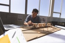 Vista frontal do arquiteto masculino asiático trabalhando em um modelo arquitetônico na mesa em um escritório moderno — Fotografia de Stock