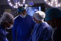 Visão frontal dos cirurgiões conversando entre si durante a cirurgia na sala de cirurgia do hospital — Fotografia de Stock